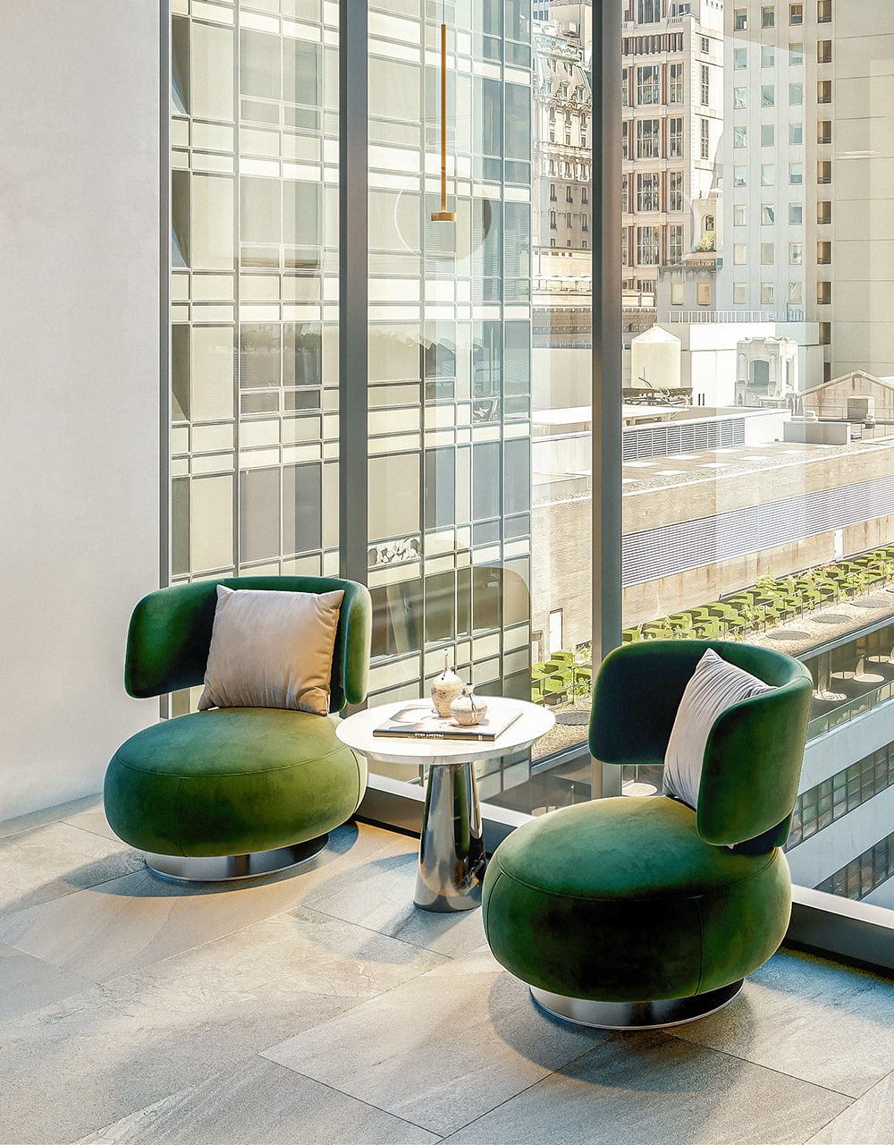 Two dark green designer seats in front of a window in a big city